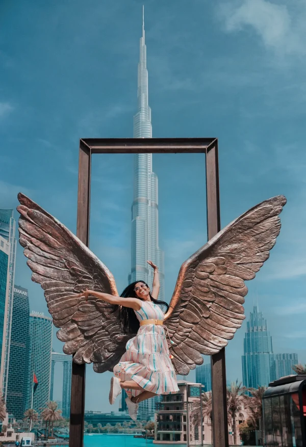 A woman Sanmita in a dress poses gracefully beside a Wings Of Mexico, with Burj Khalifa in the background capturing a serene moment in a picturesque setting.